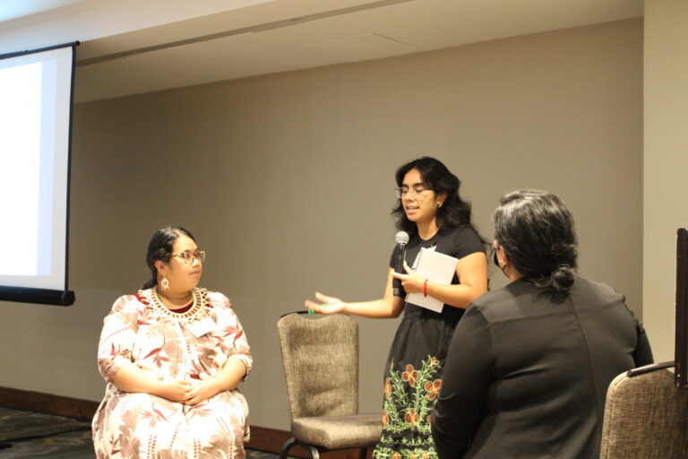 Cassandra Micah speaking and Philmar Kabua-Mendoza and Michelle Pedro sitting facing Cassandra Micah.